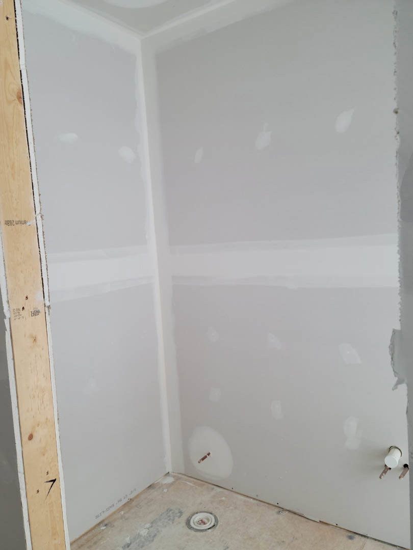 White plaster wall with circular cutouts, smooth surface, and light-colored flooring in a modern interior room.