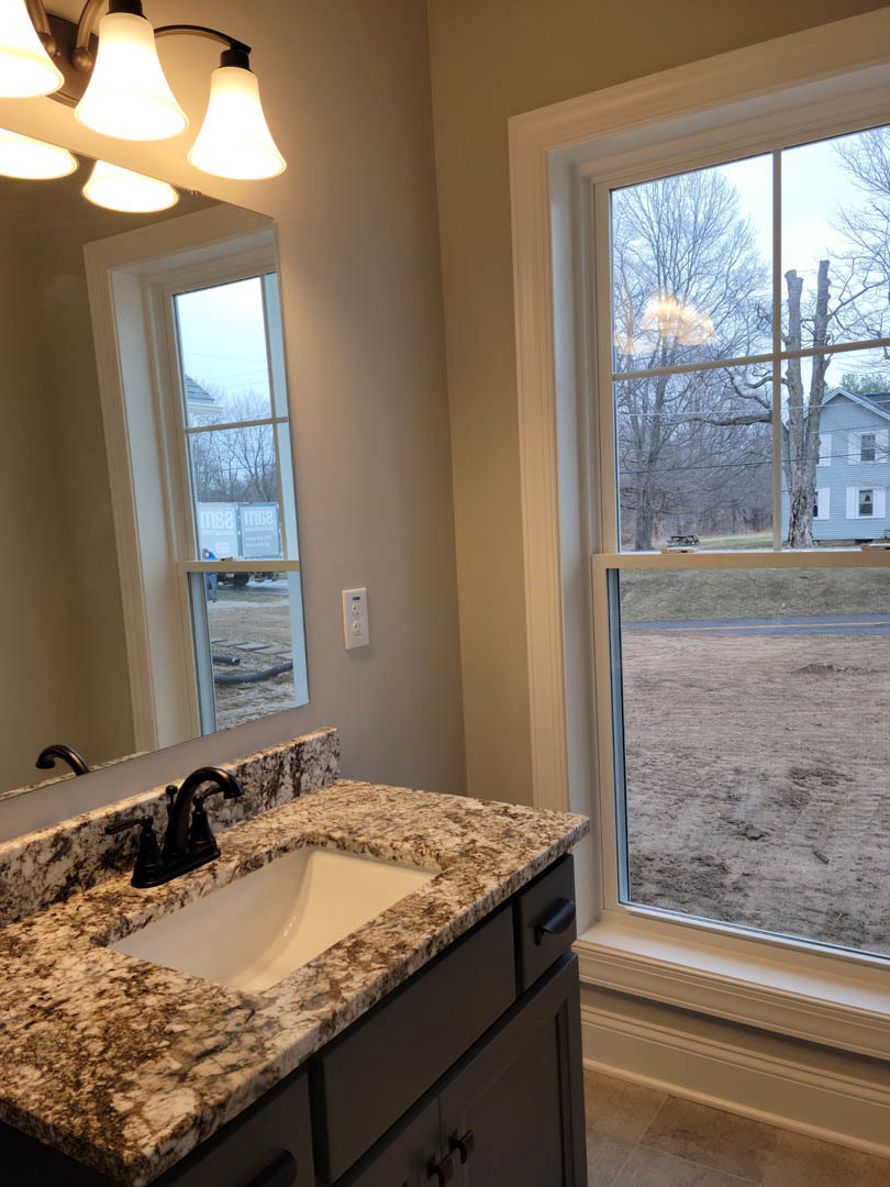 White quartz countertop with undermount sink, chrome faucet, rectangular tile backsplash, wood cabinetry, and large window overlooking sandy landscape