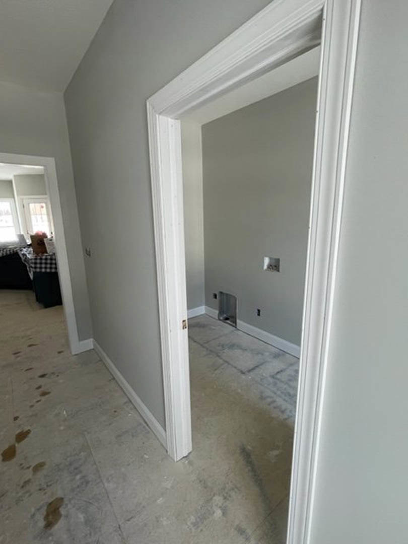 White plaster wall with doorway leading to tiled bathroom, dirty floor in foreground, black and white checkered tablecloth partially visible.