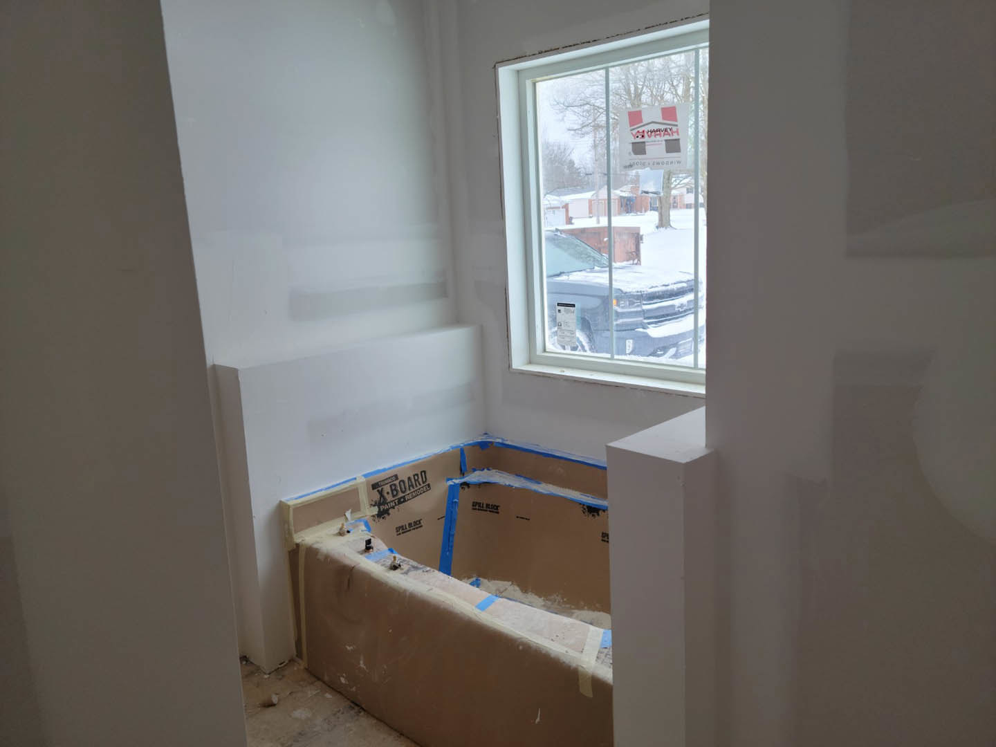 Freestanding white bathtub beneath large window, smooth plaster walls, natural light illuminating bathroom interior