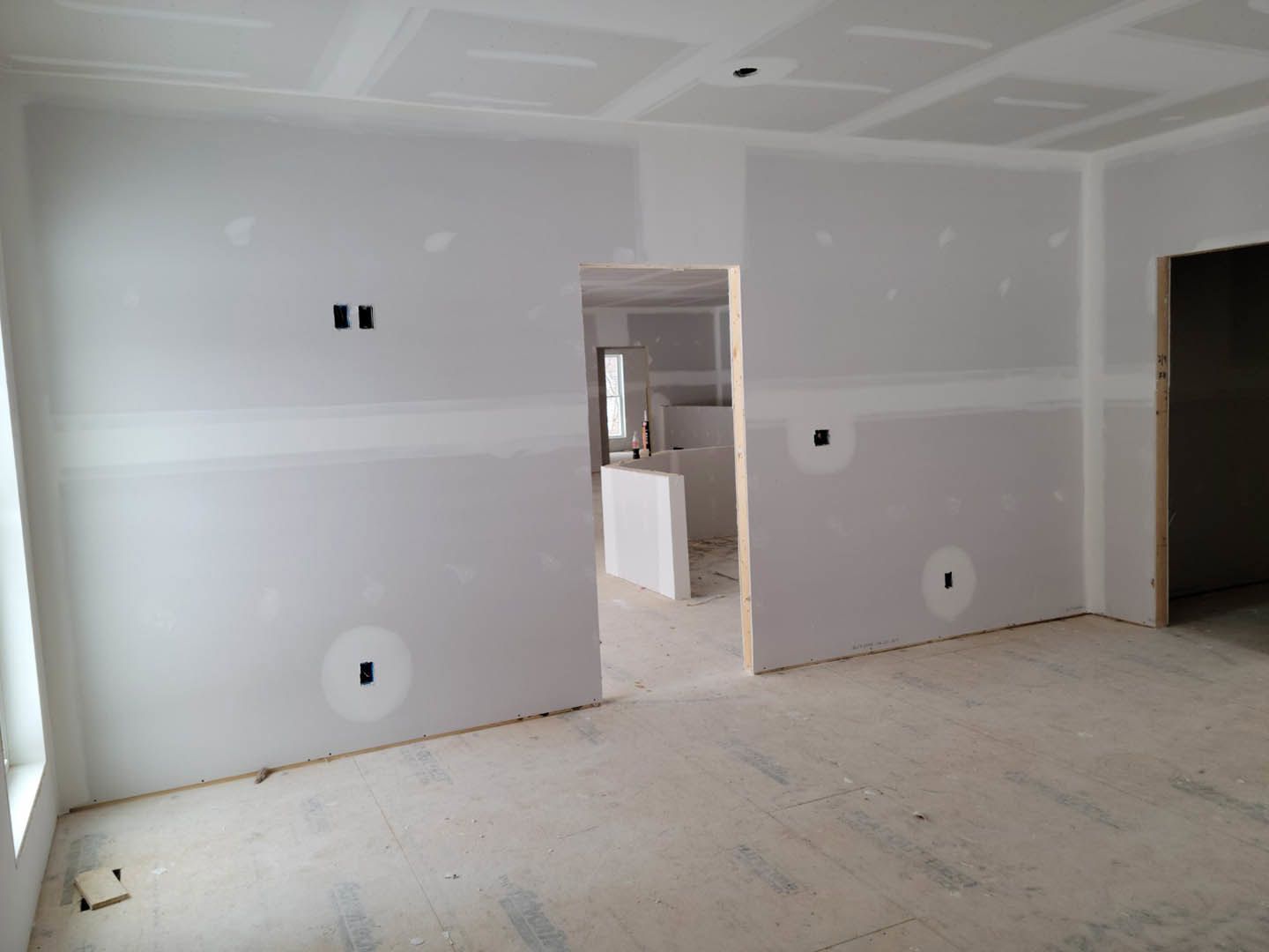 White-walled room with light wood flooring, white ceiling, and a single white door featuring a black handle