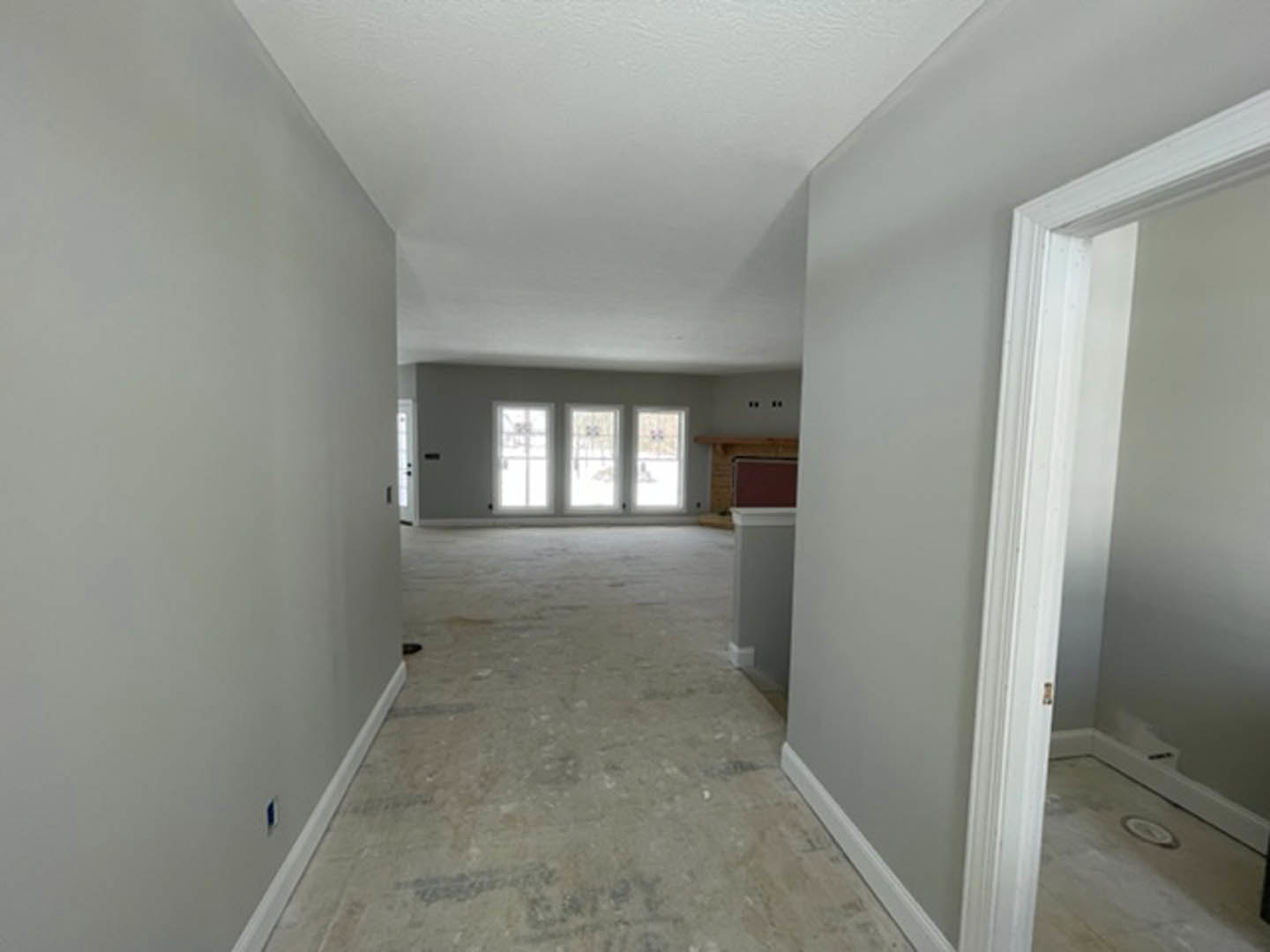 Hallway with smooth white plaster walls, white door, concrete flooring, row of windows letting in natural light