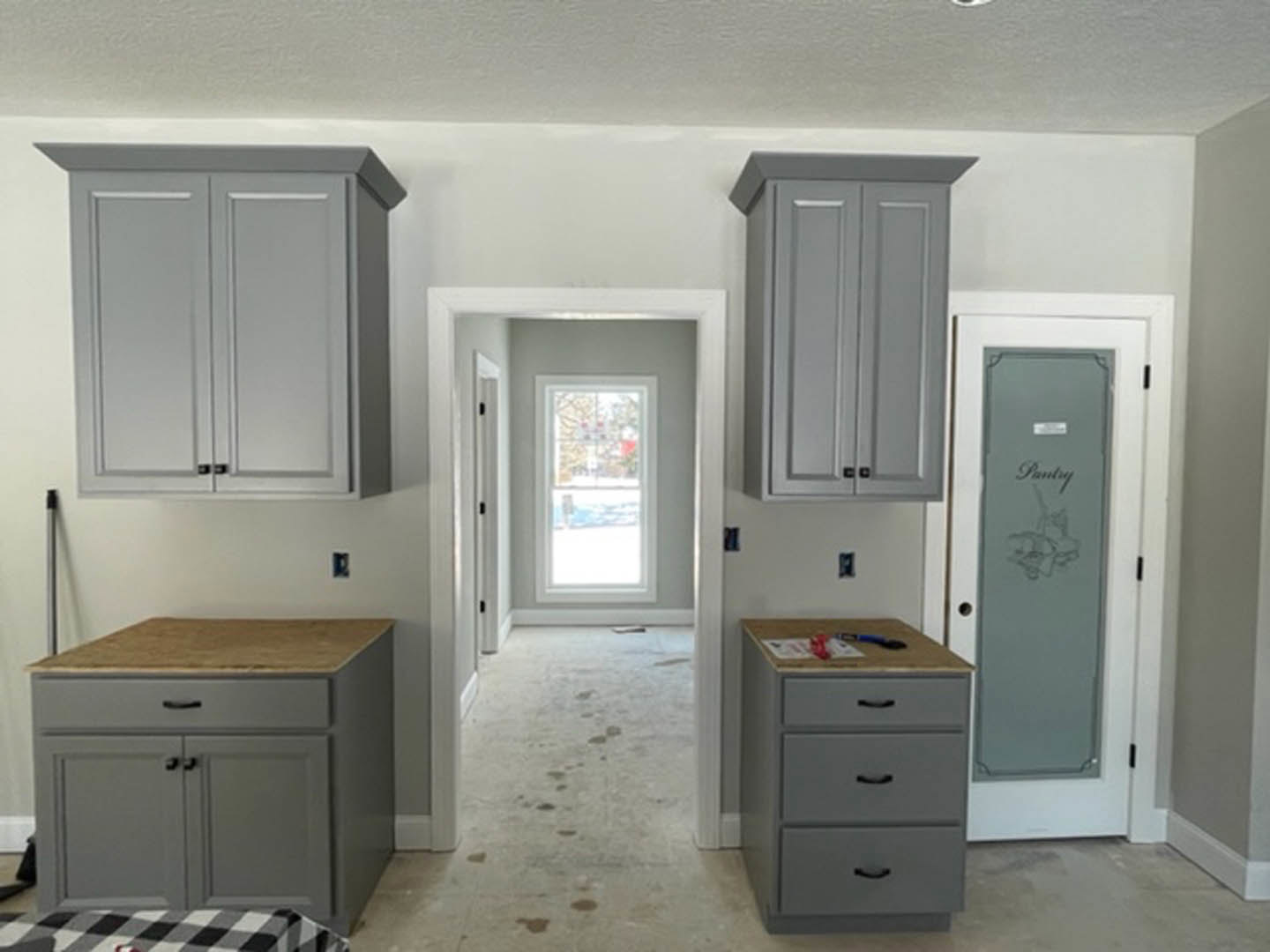 Modern kitchen featuring grey cabinets with black handles, wooden countertops, stainless steel sink, and a window overlooking the street; black and white checkered fabric accents