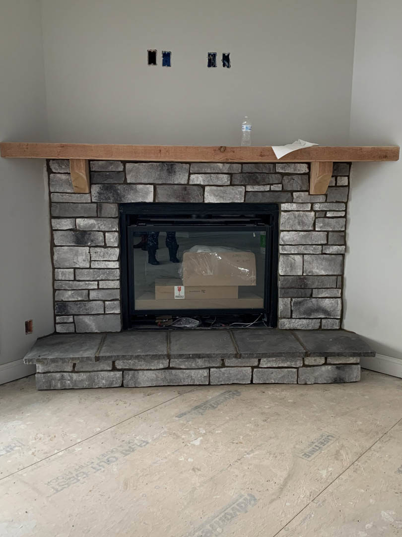 Stone fireplace with glass door, built-in hearth shelf, and wood flooring in a modern living room