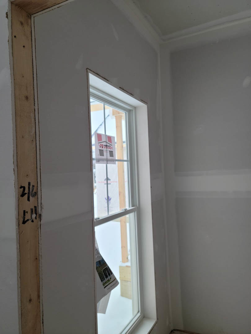 White-framed window set in a white plaster wall, wood paneling below, black house numbers on a white surface nearby