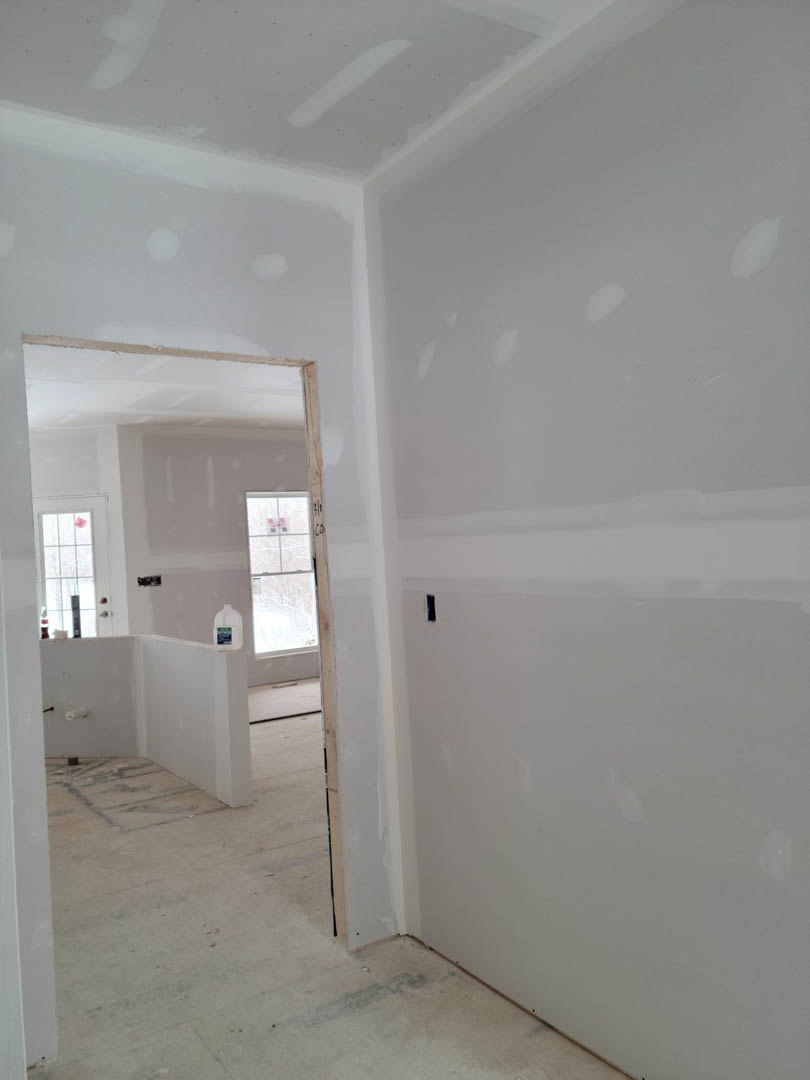 Open white door leading to adjacent room with white plaster walls, light wood flooring, and window with white frame; pink ceiling fan visible through window.