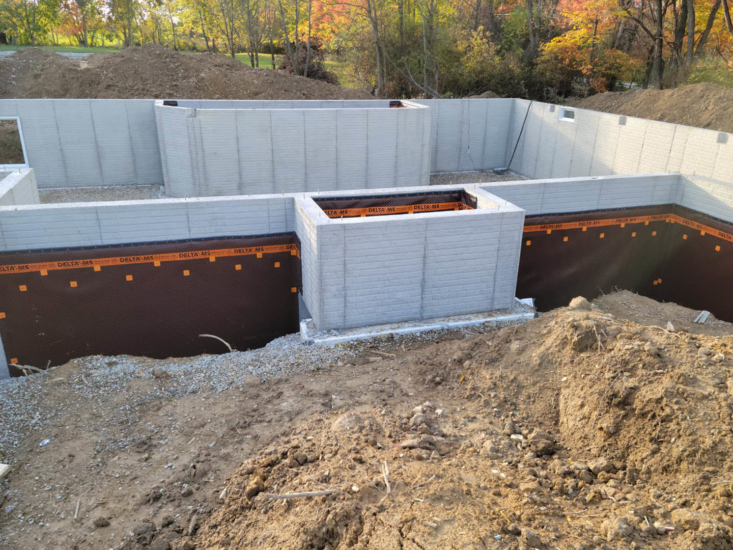 Concrete foundation with open doorway, adjacent dirt hill, partial fence, and surrounding trees