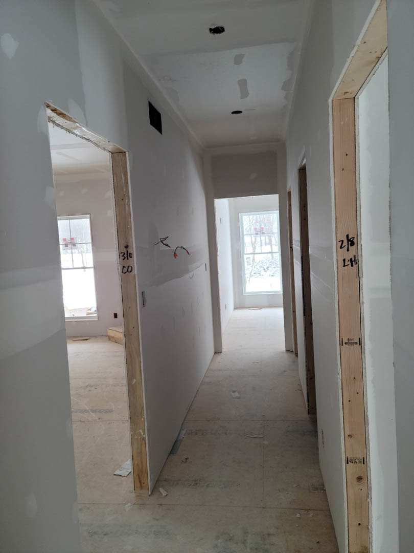 Hallway with smooth white plaster walls, light wood flooring, doorway, and large window overlooking snowy landscape