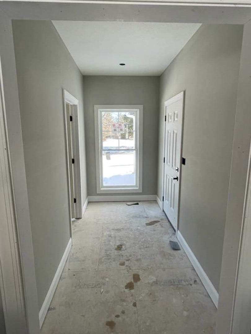 Hallway with white plaster walls, molding, a window with a sign visible outside, and a white door; dirty flooring with scattered dirt.
