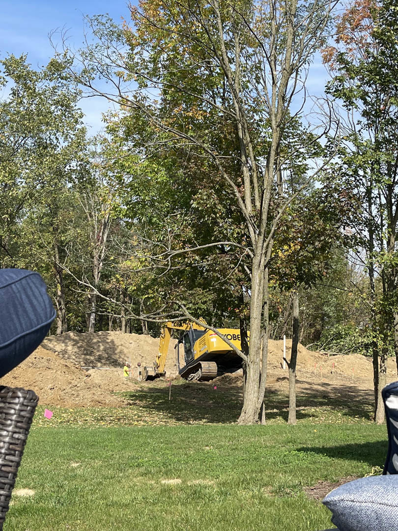 Yellow bulldozer parked in a dirt pit surrounded by trees and grass under a clear sky