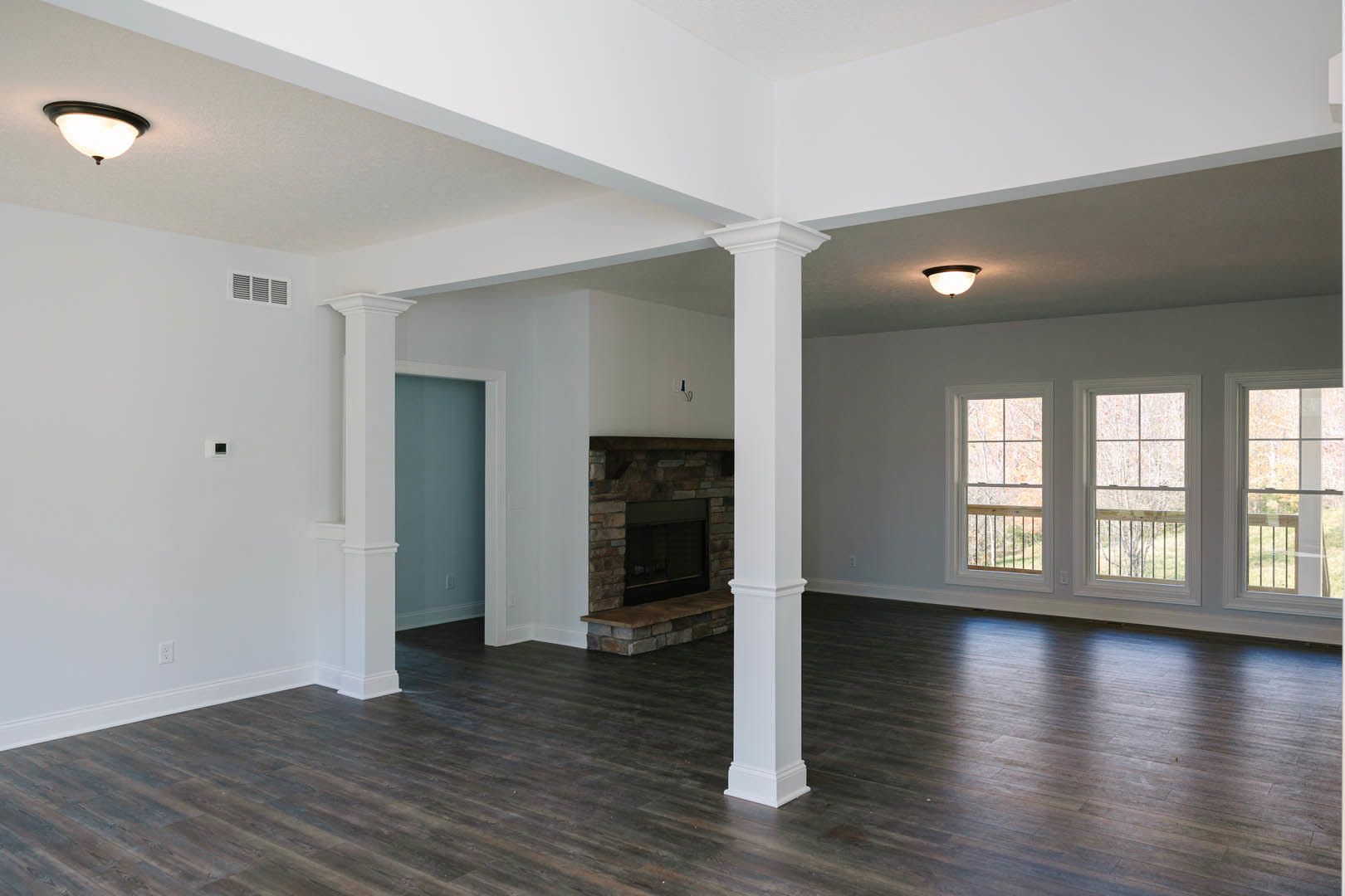 Living room with white pillars, stone fireplace, wood flooring, row of windows with railings, and round light fixture on ceiling