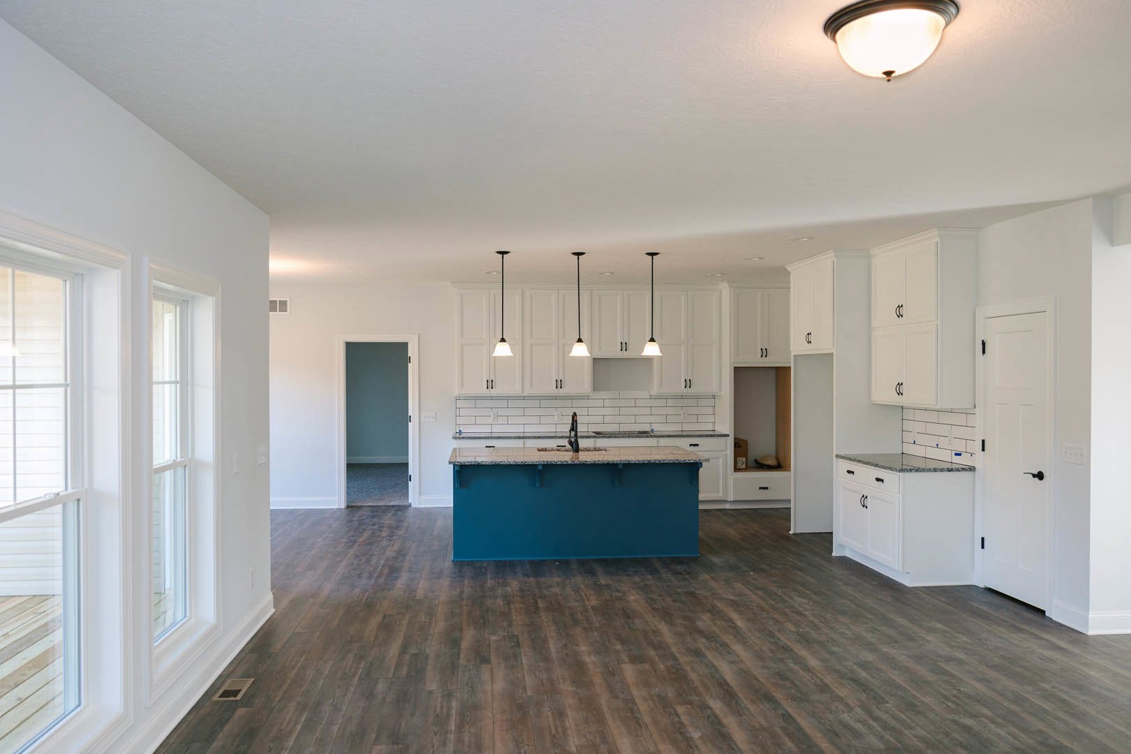 Blue kitchen island with white shaker cabinets, quartz countertops, wood flooring, ceiling light fixture, and stainless steel sink