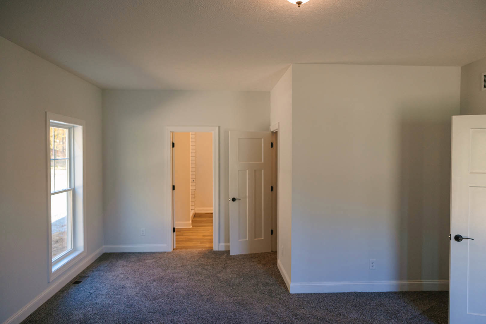 Carpeted room with two white doors, black and white handles, white walls, and a window.