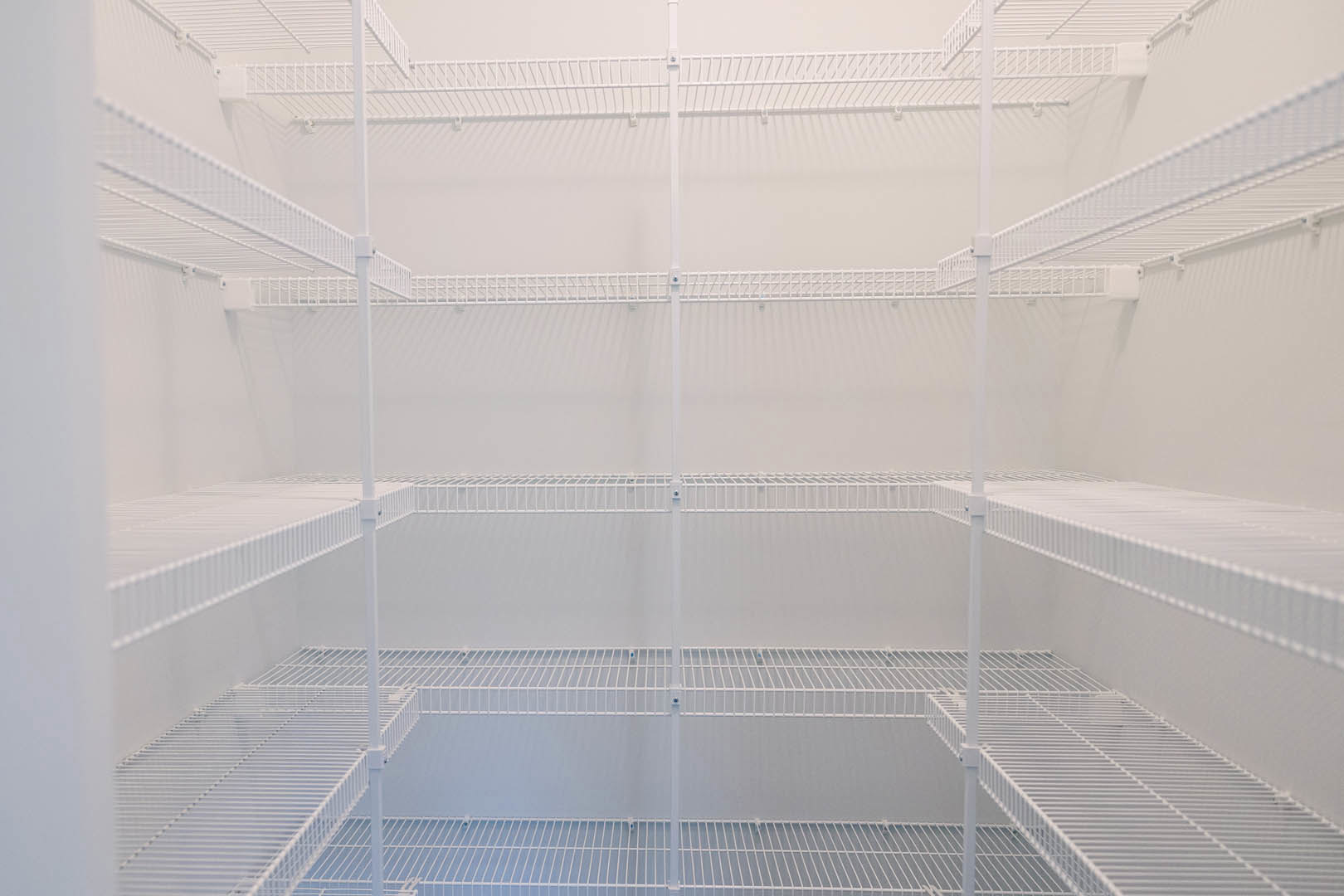 White wire shelf mounted on a wall in a large empty room with white walls and white metal railing