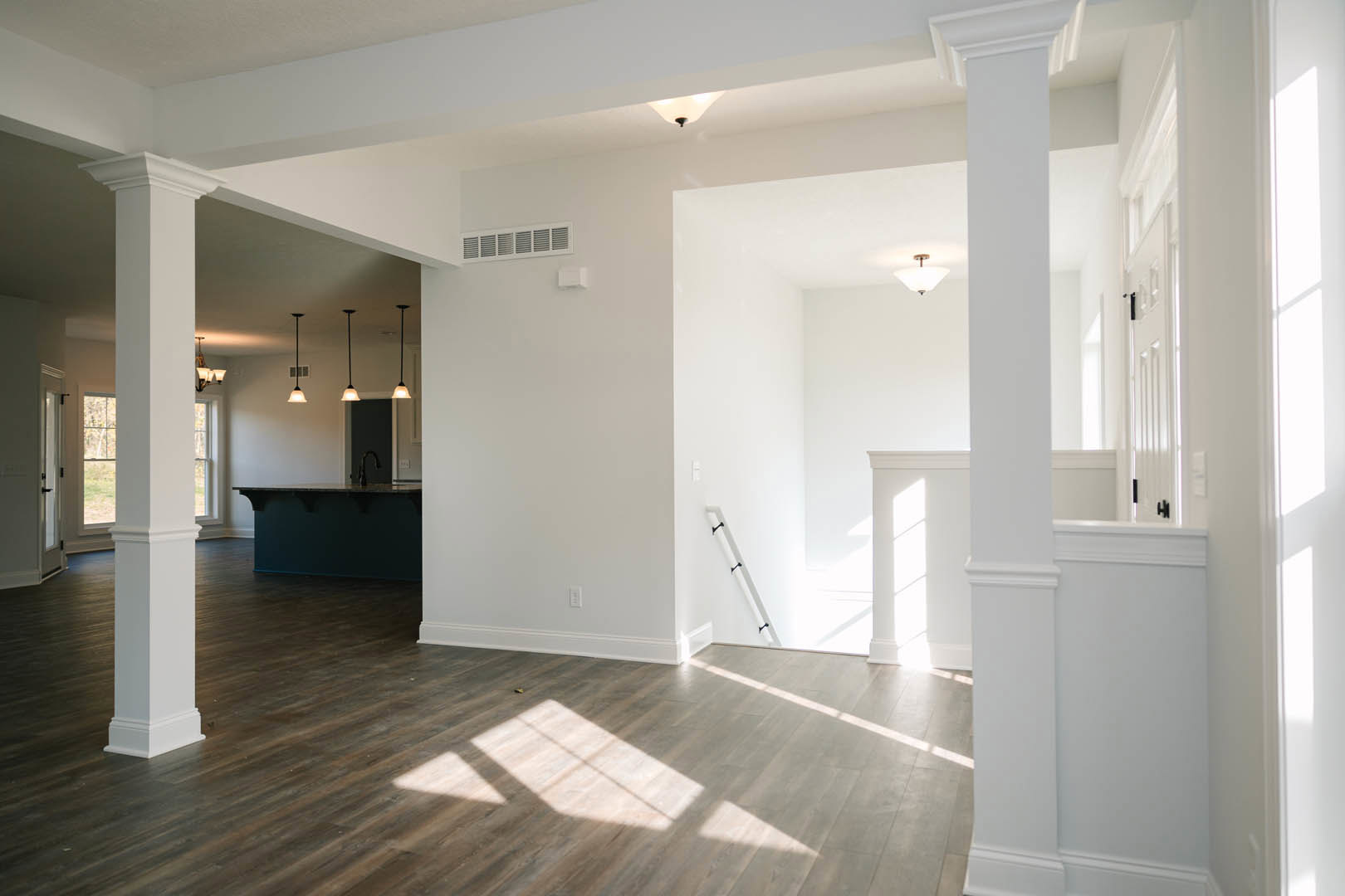 Open-concept room with light wood flooring, white walls, black accents, modern staircase, recessed ceiling lights, and partial view of kitchen area