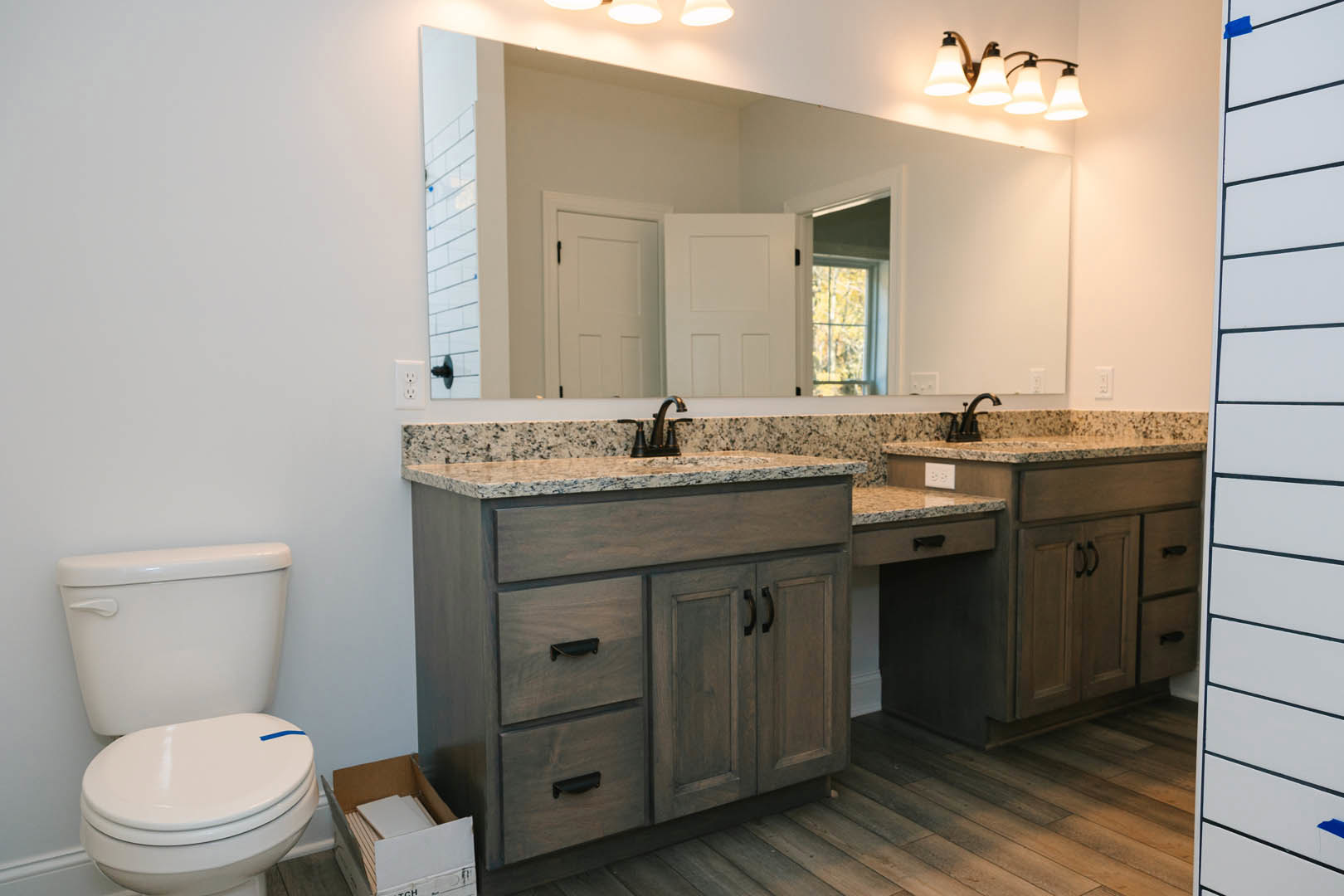 Modern bathroom featuring a white vanity with sink, wall-mounted mirror, chrome faucet, white cabinet, toilet with blue tape, and contemporary light fixture.