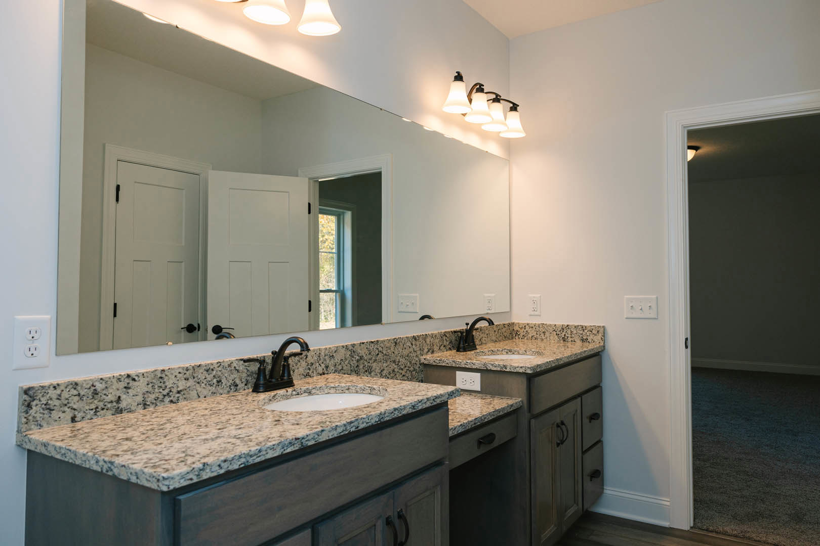 Bathroom featuring a marble countertop with undermount sink, expansive wall-mounted mirror, modern light fixture above, white electrical outlet and multi-switch panel on tiled
