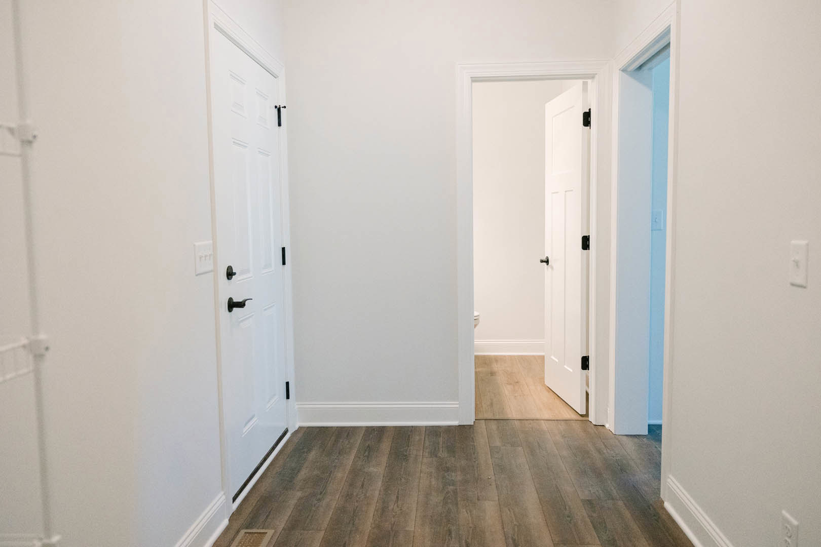 Hallway with white walls and doors, wood flooring, white door with silver handle, black object mounted on wall