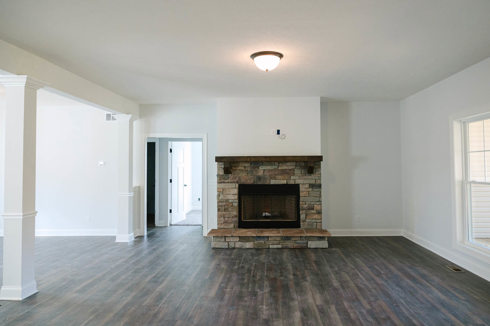 Modern fireplace with glass door set in a white wall, wood flooring, black-handled white door, and decorative molding in a den