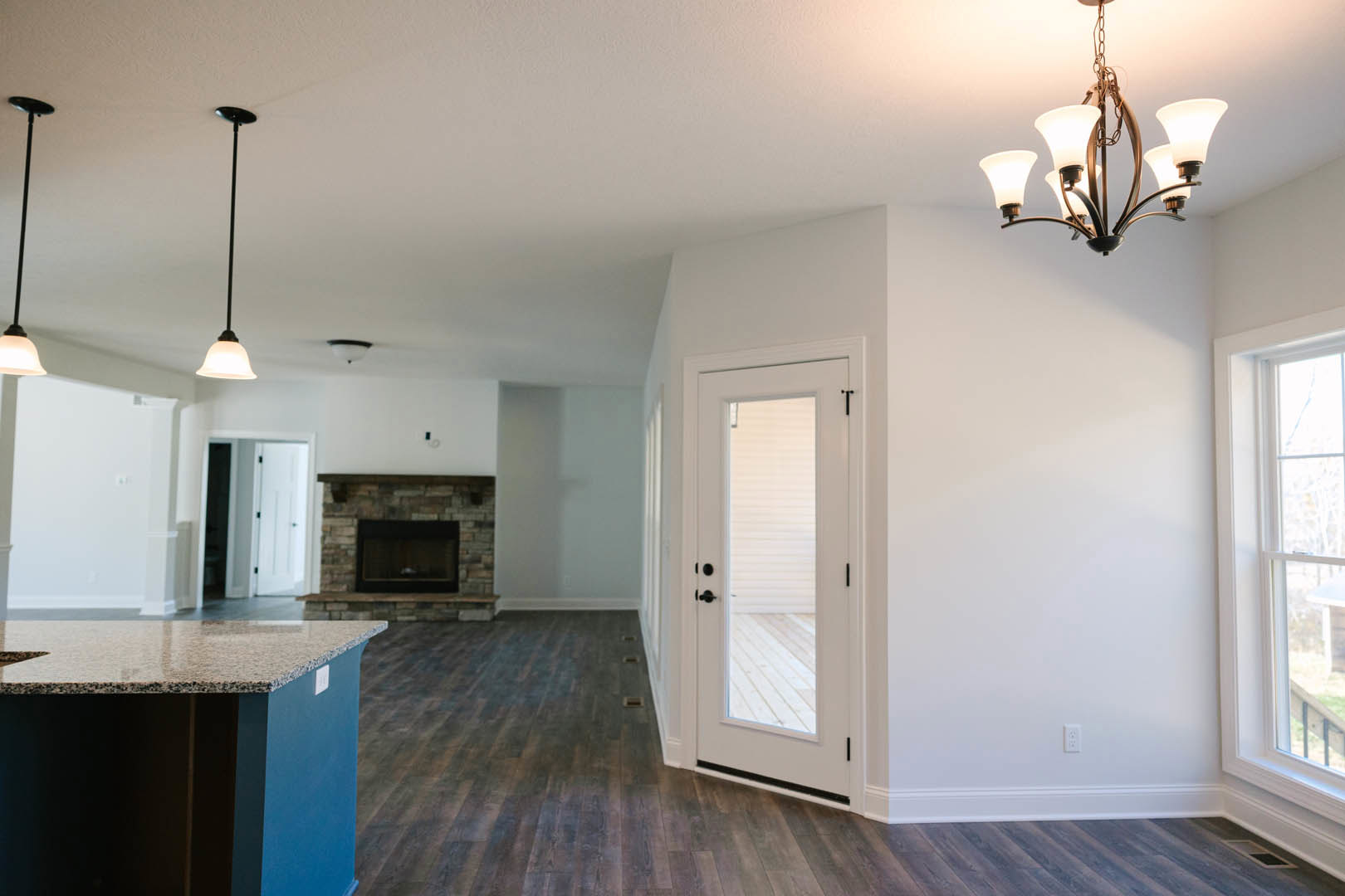 Living room with stone fireplace, white door with black handles, blue accent wall, modern chandelier, hardwood flooring, and built-in shelving.