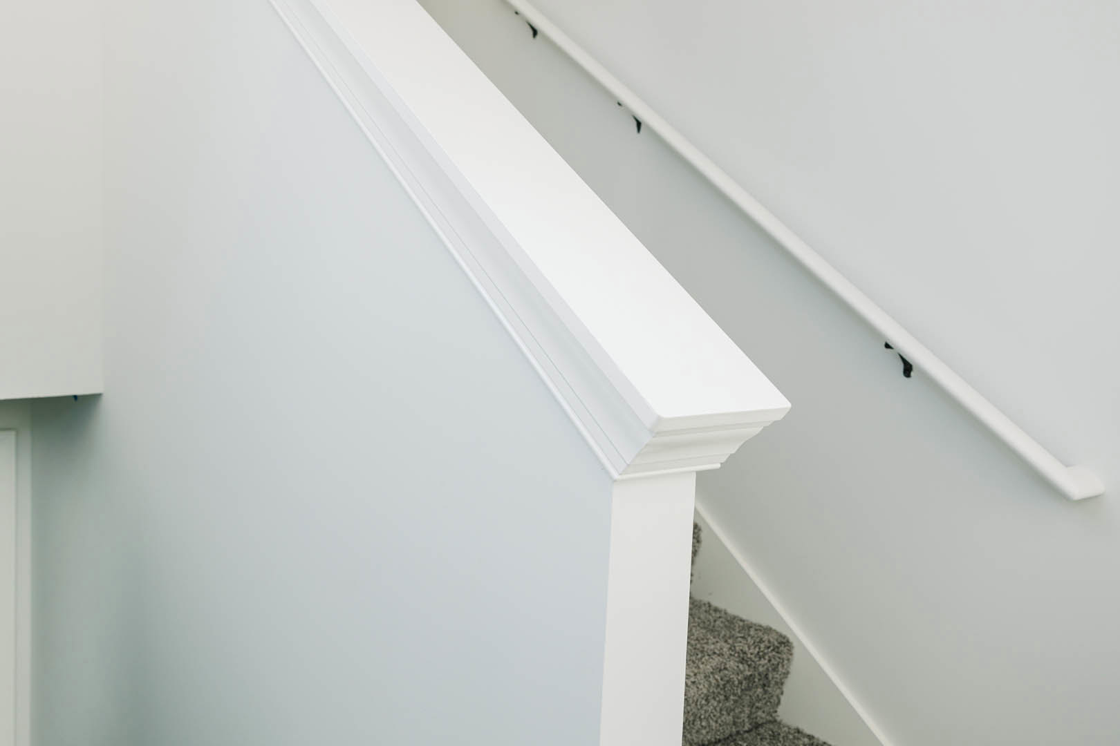 White-painted staircase railing with carpeted steps and smooth white plaster wall in a residential interior.