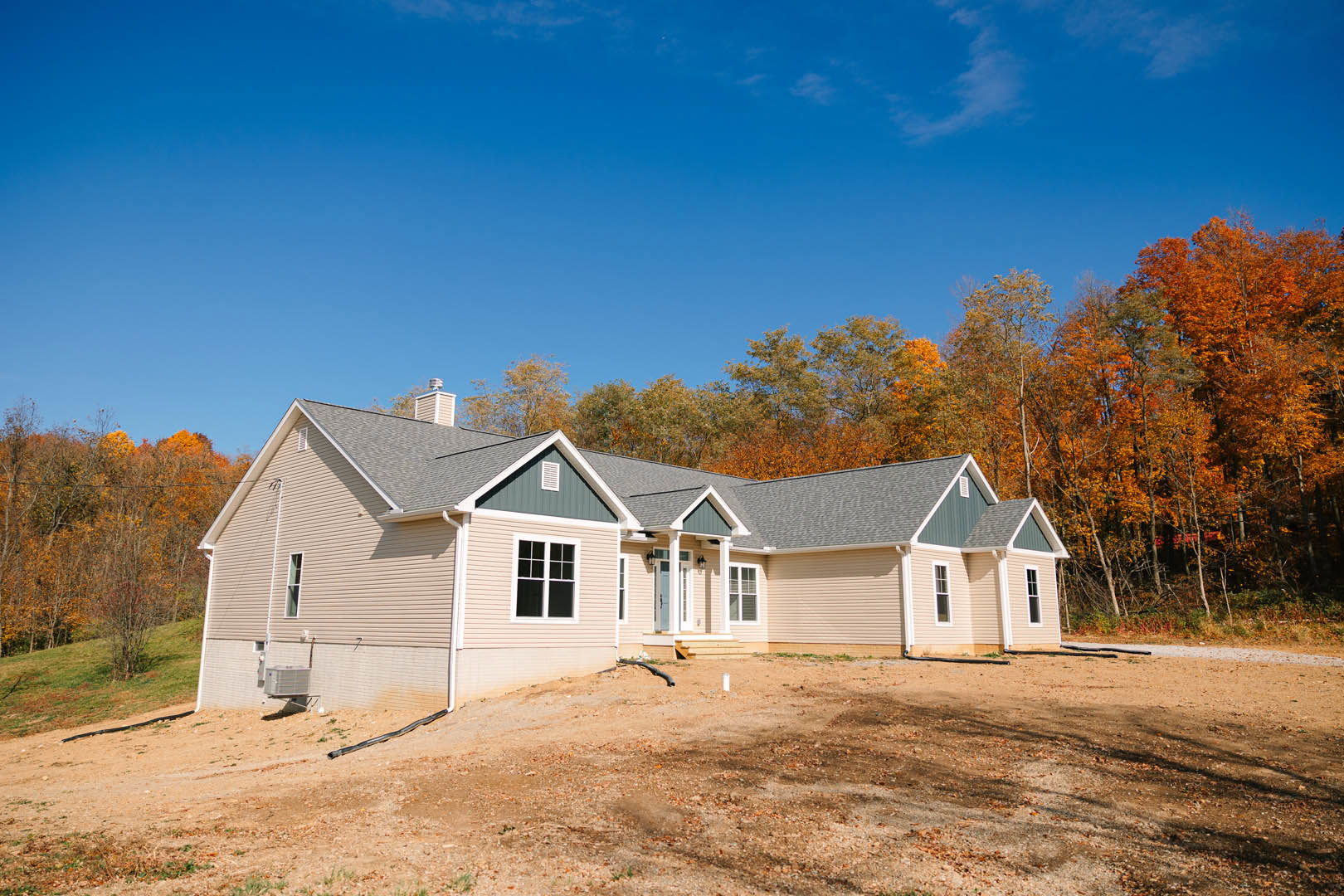 Two-story cottage with multi-pane windows, white siding, and a sloped roof, surrounded by autumn trees with orange leaves under a clear blue sky