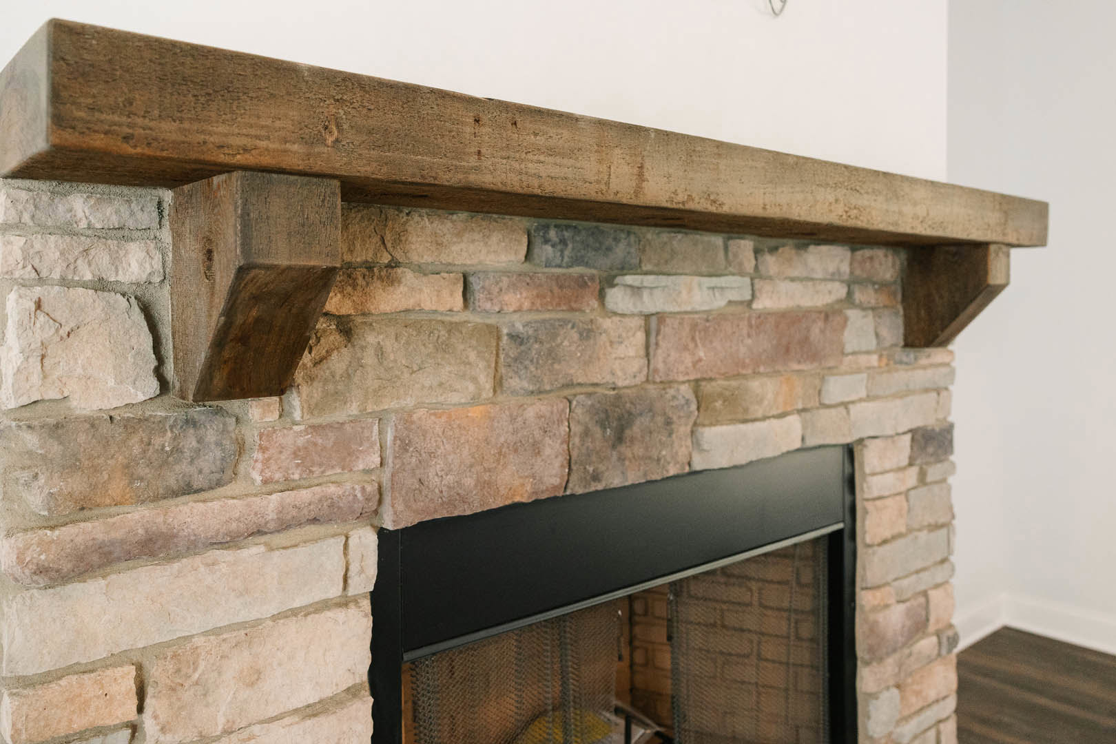 Stone fireplace with black metal border, topped by a rustic wood beam mantel, set against a brick accent wall.