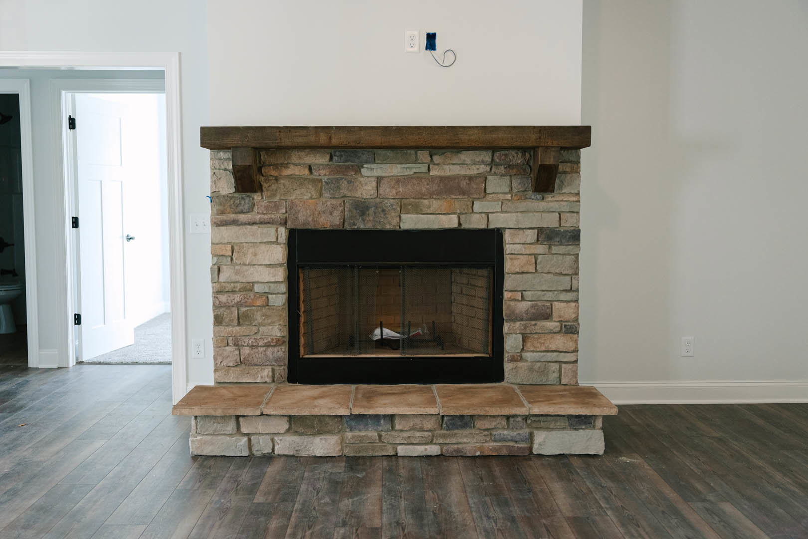 Stone fireplace with wire mesh screen, wood-burning stove, and stone hearth; white door with silver handle visible in background; bird figurine inside fireplace cage.