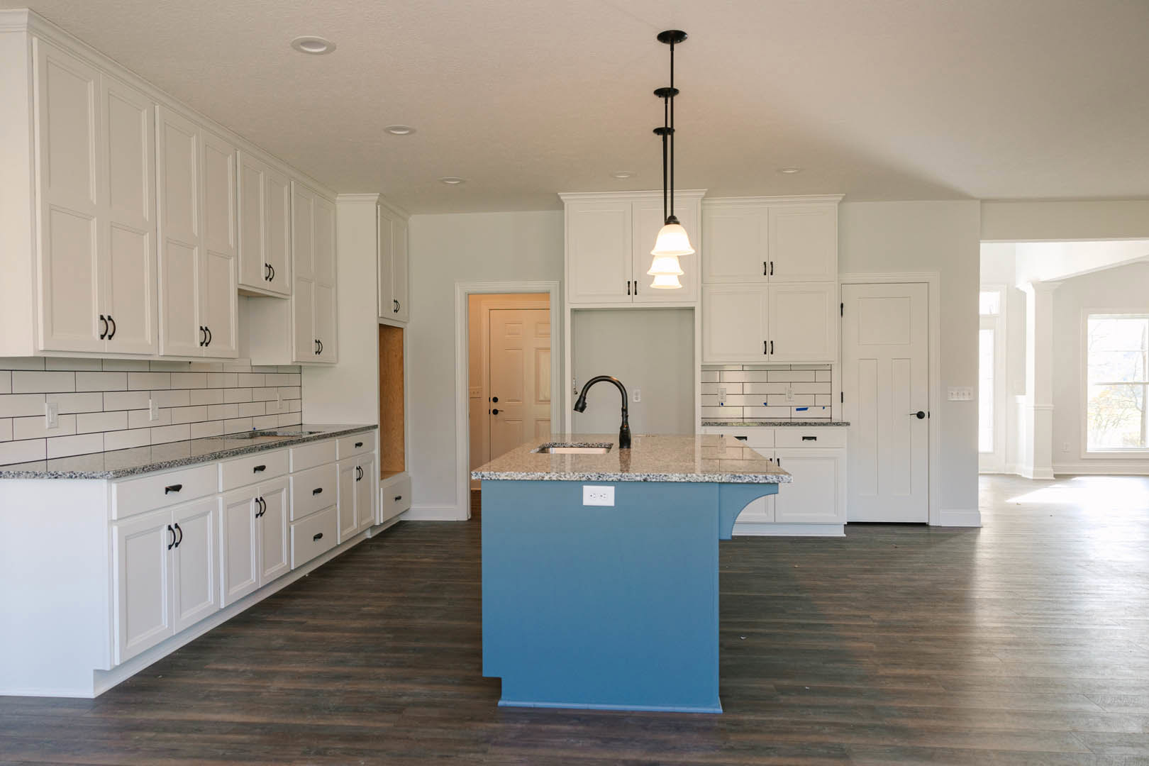 Blue kitchen island with marble countertop, white shaker cabinets, black faucet, pendant lighting, stainless steel appliances, and light tile flooring