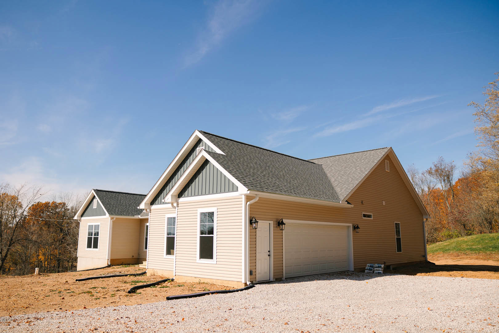 Two-story house with gray siding, white-framed windows, attached garage featuring illuminated white door, black pipe along driveway, white entry door with black hardware, shingled