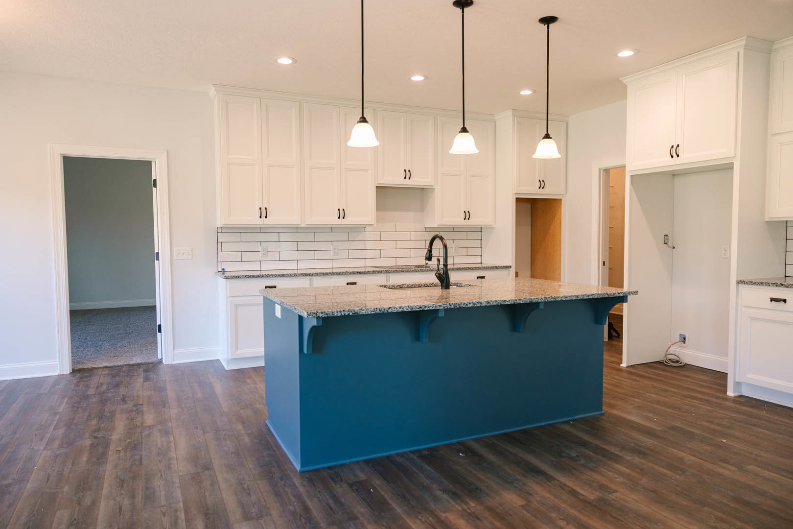 Blue kitchen island with white countertop, stainless steel sink, white cabinetry, tile backsplash, wood flooring, and modern pendant light fixtures