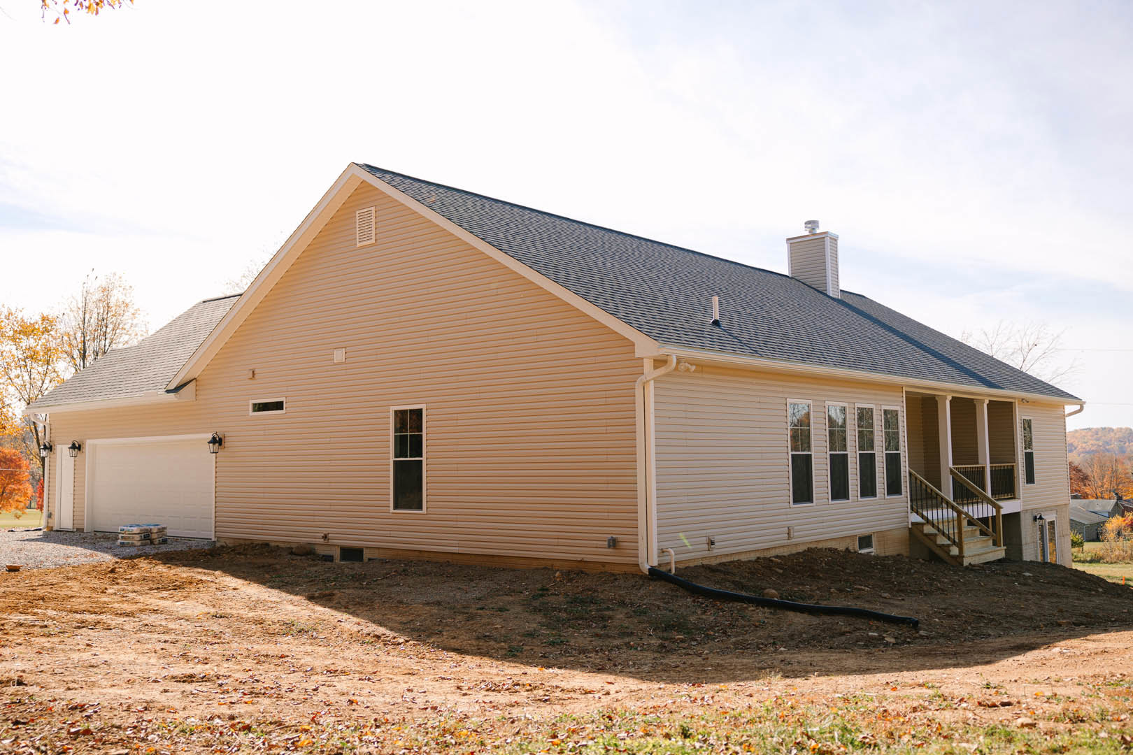 Modern two-story home with gray siding, attached two-car garage, concrete driveway, large front windows, gable roof, and landscaped yard with young trees