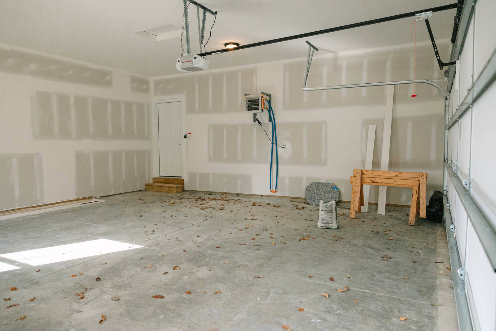 Wood table with sturdy legs set on light flooring, surrounded by scattered tools and leaves; plaster walls and ceiling visible, vent and bag of food nearby.
