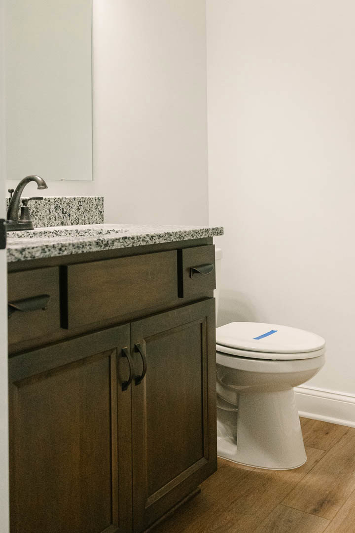 Bathroom with marble countertop and sink, chrome faucet, toilet featuring blue tape across seat, white tile walls, partial view of a bag on the floor