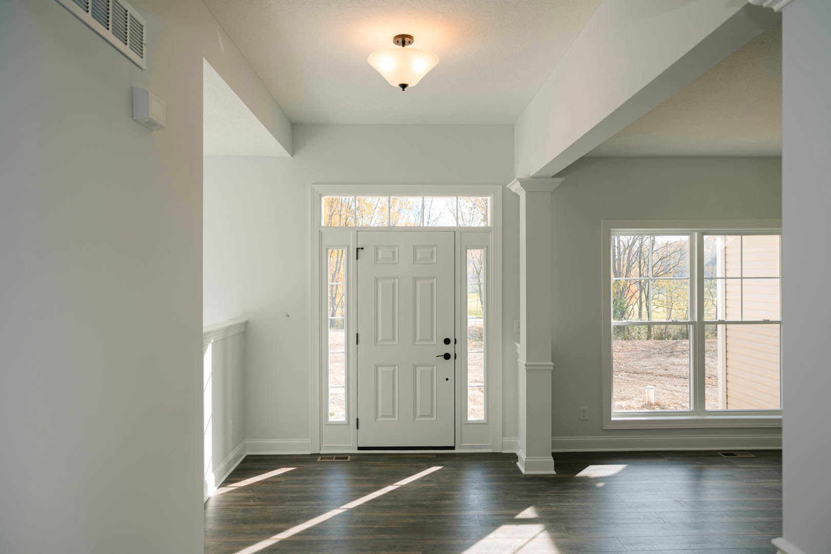 White paneled door with black handles set in a white wall with matching trim, wooden laminate flooring, and a window overlooking a green yard.