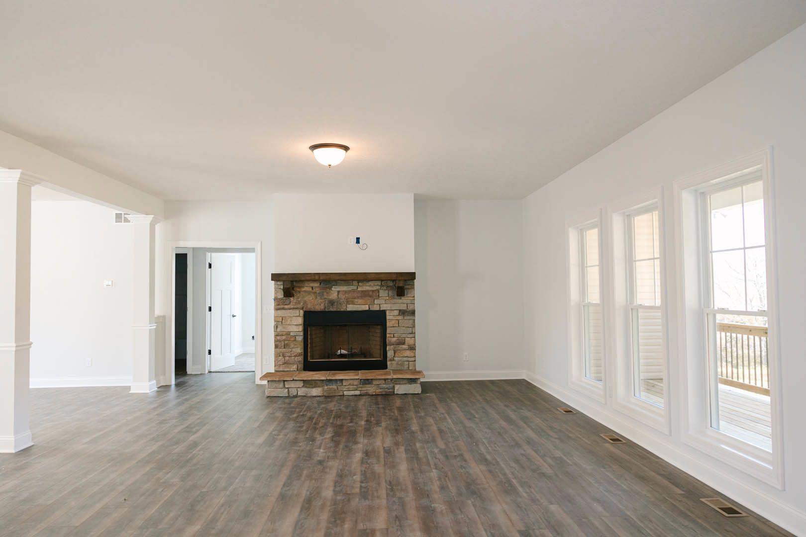 Living room with glass-door fireplace, light hardwood floors, white plaster walls, and large window featuring a black rectangular object.