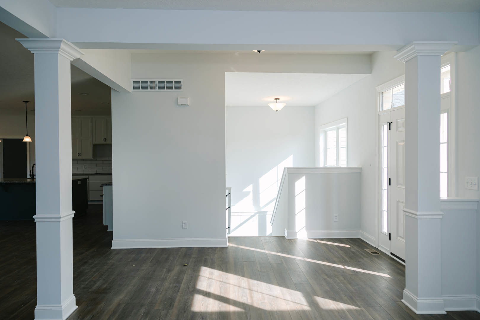 Sunlit room with white plaster walls, natural hardwood flooring, white-shaded ceiling light fixture, and close-up of floor vent