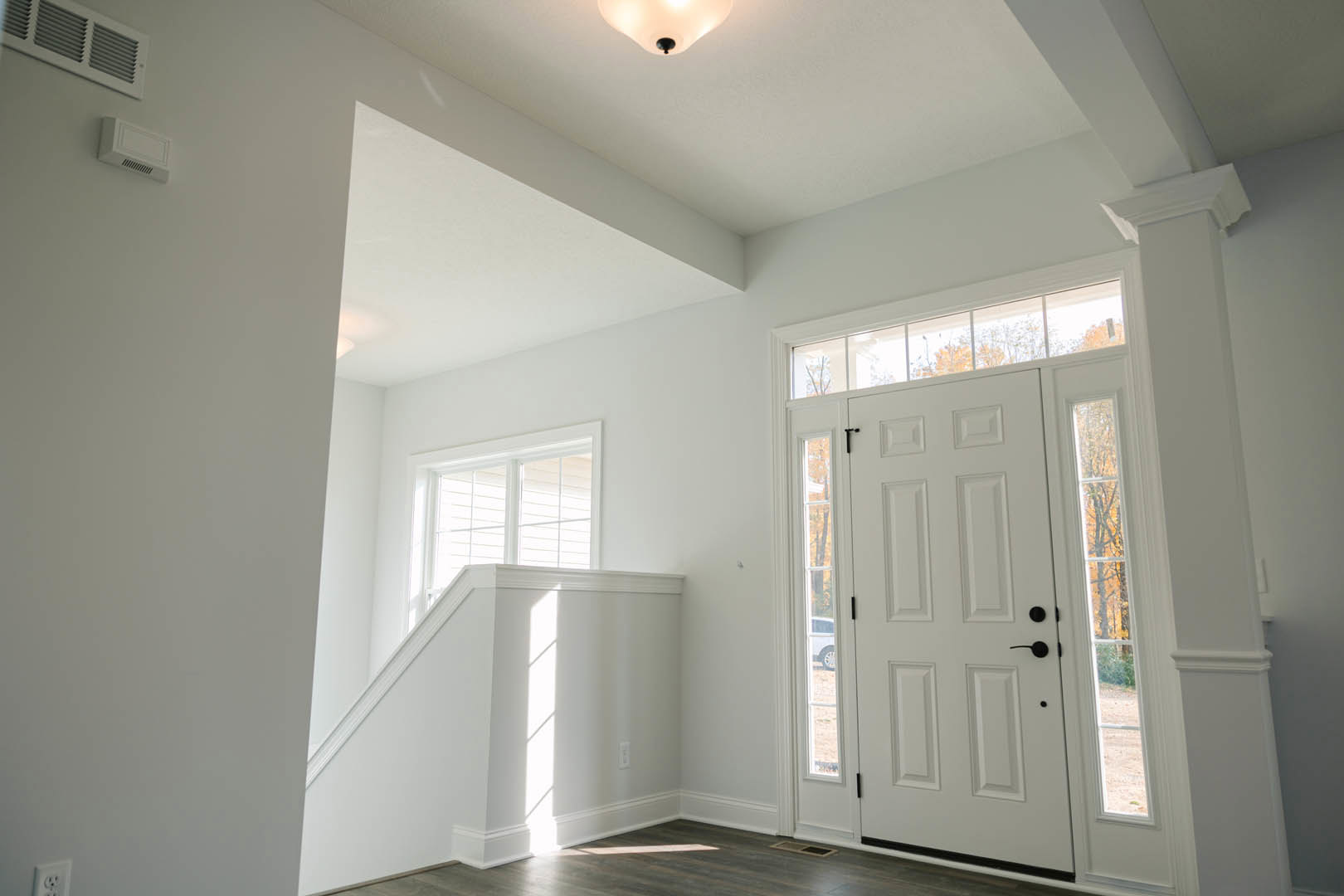 White-walled room featuring a staircase, white door with black handles, wall vent, recessed ceiling light, window, and white baseboard molding.