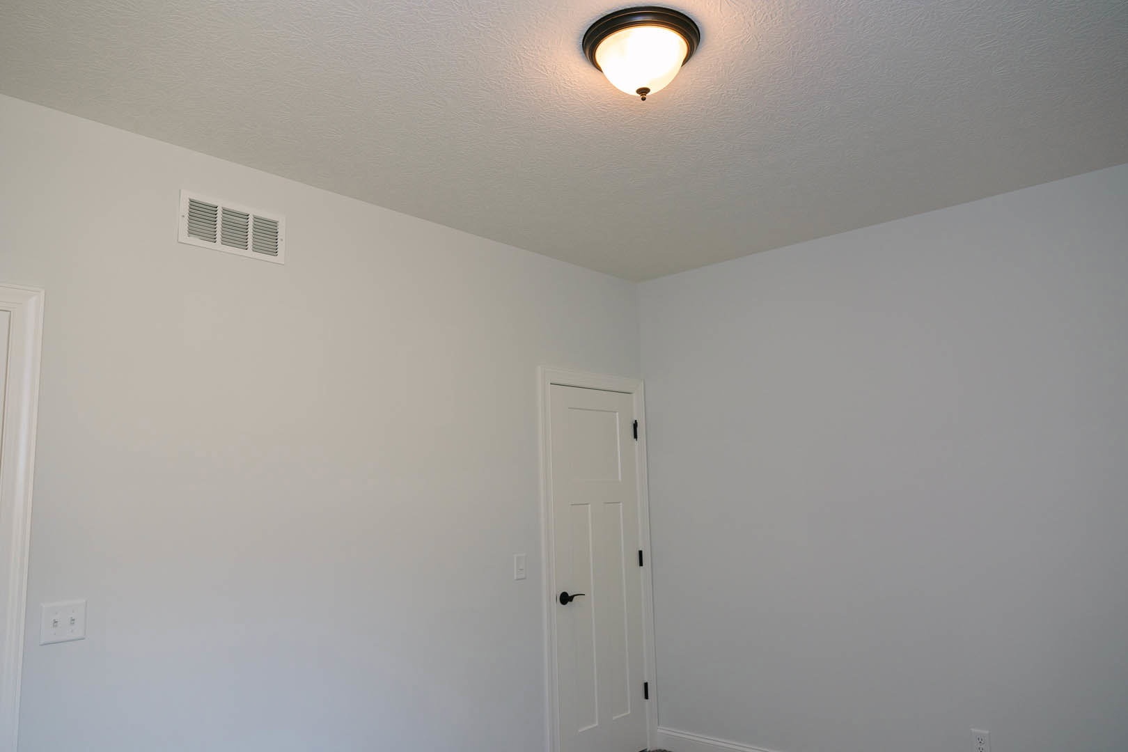 White door with black handle beneath a ceiling-mounted light fixture in a white plaster room, vent visible on ceiling