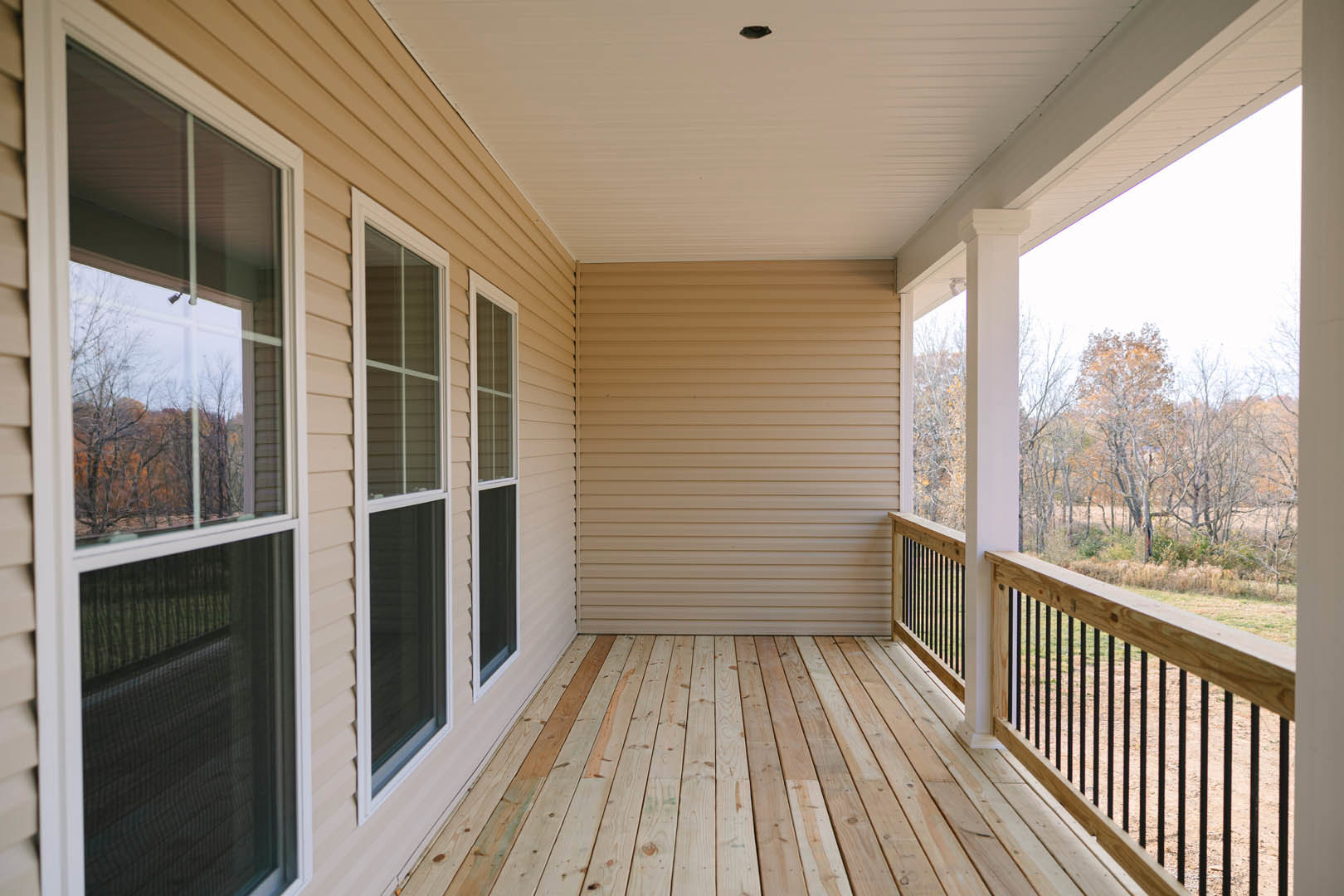 Wooden deck with black metal railing, large windows framed in white, forest view through glass, white exterior wall