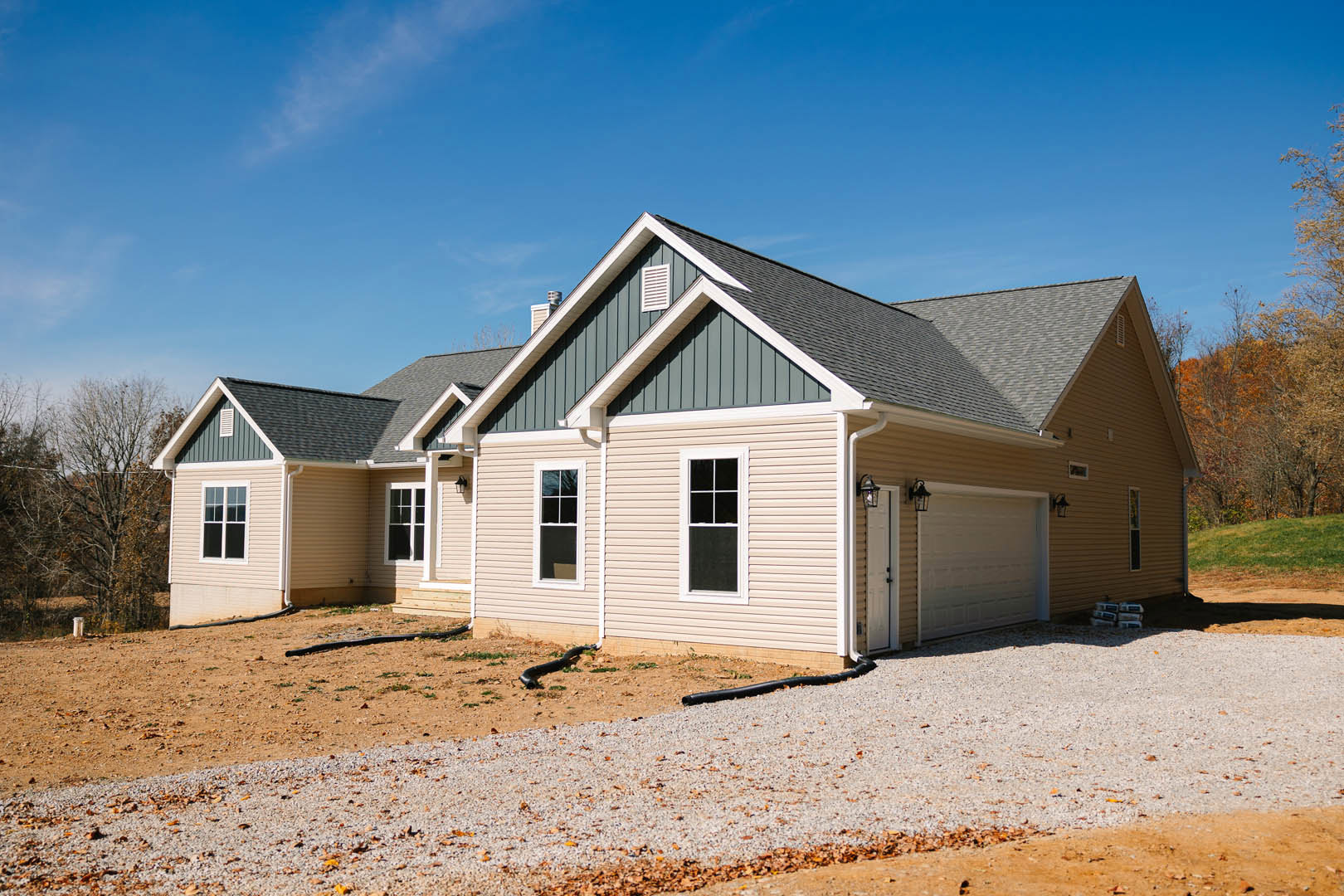 Modern home with gray siding, white-framed windows, attached garage, asphalt driveway, gravel border, and black downspout; small black lizard visible near foundation.