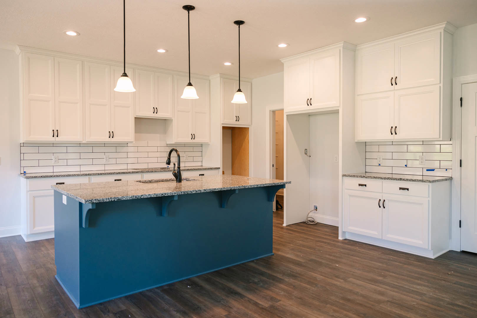 Blue kitchen island with marble countertop, white shaker cabinets, stainless steel faucet over undermount sink, pendant light fixture, light hardwood flooring, white walls