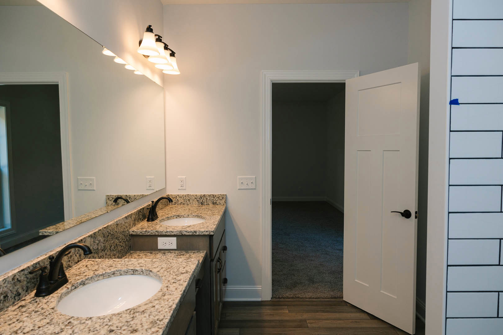 Bathroom with marble countertops, undermount sink, chrome faucet, white tile walls, and a wooden door