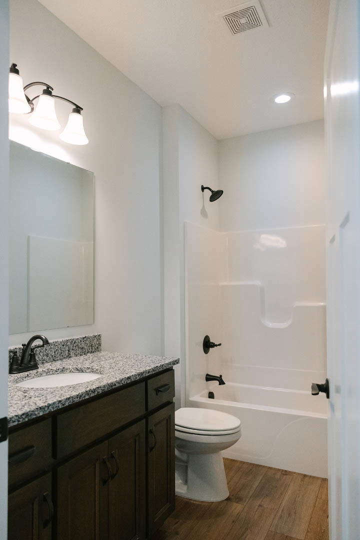 Modern bathroom featuring a white ceramic sink with chrome faucet, glass-enclosed shower with tiled walls, light wood flooring, white cabinetry, and minimalist fixtures.