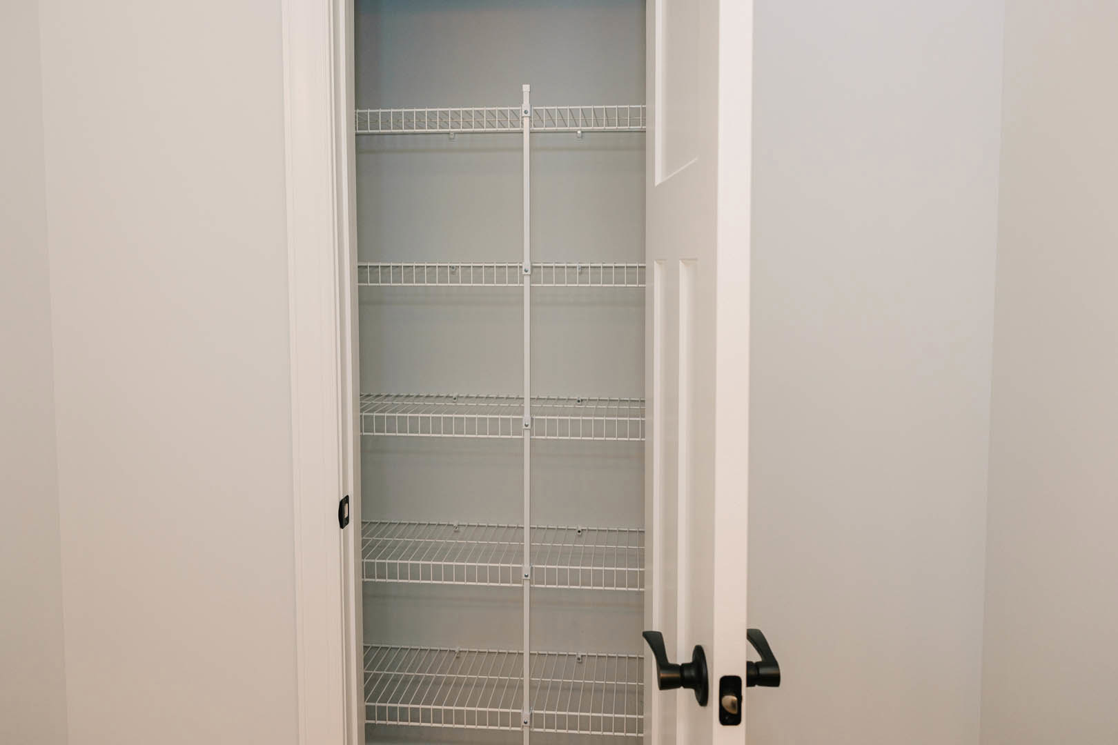 White closet door with silver handle, built-in white shelves, and metal hanging bar against light-colored walls