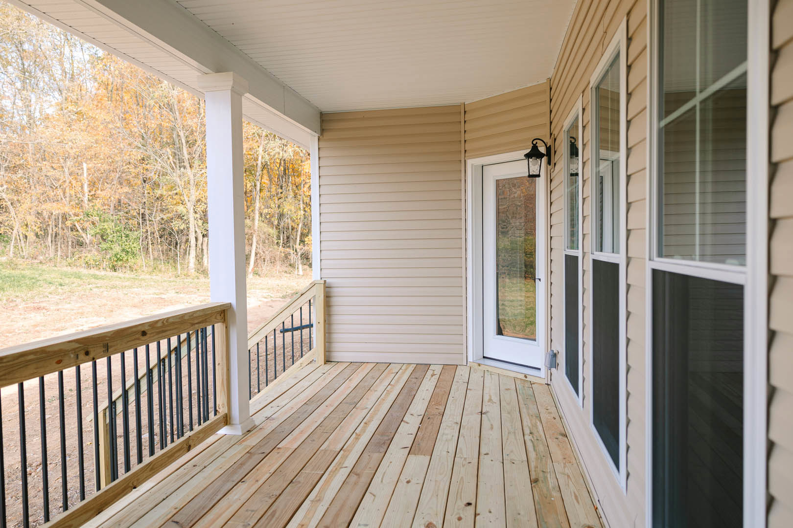 Wooden porch with metal railing, glass door with window, ceiling-mounted light fixture, and outdoor deck flooring