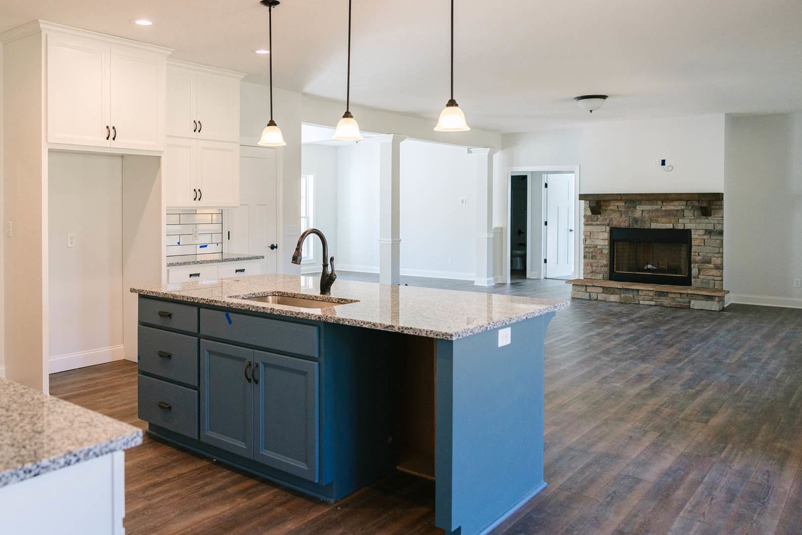 Open-concept kitchen featuring a central island with sink, white cabinetry, tile flooring, and a stone fireplace with glass window set into a white wall.