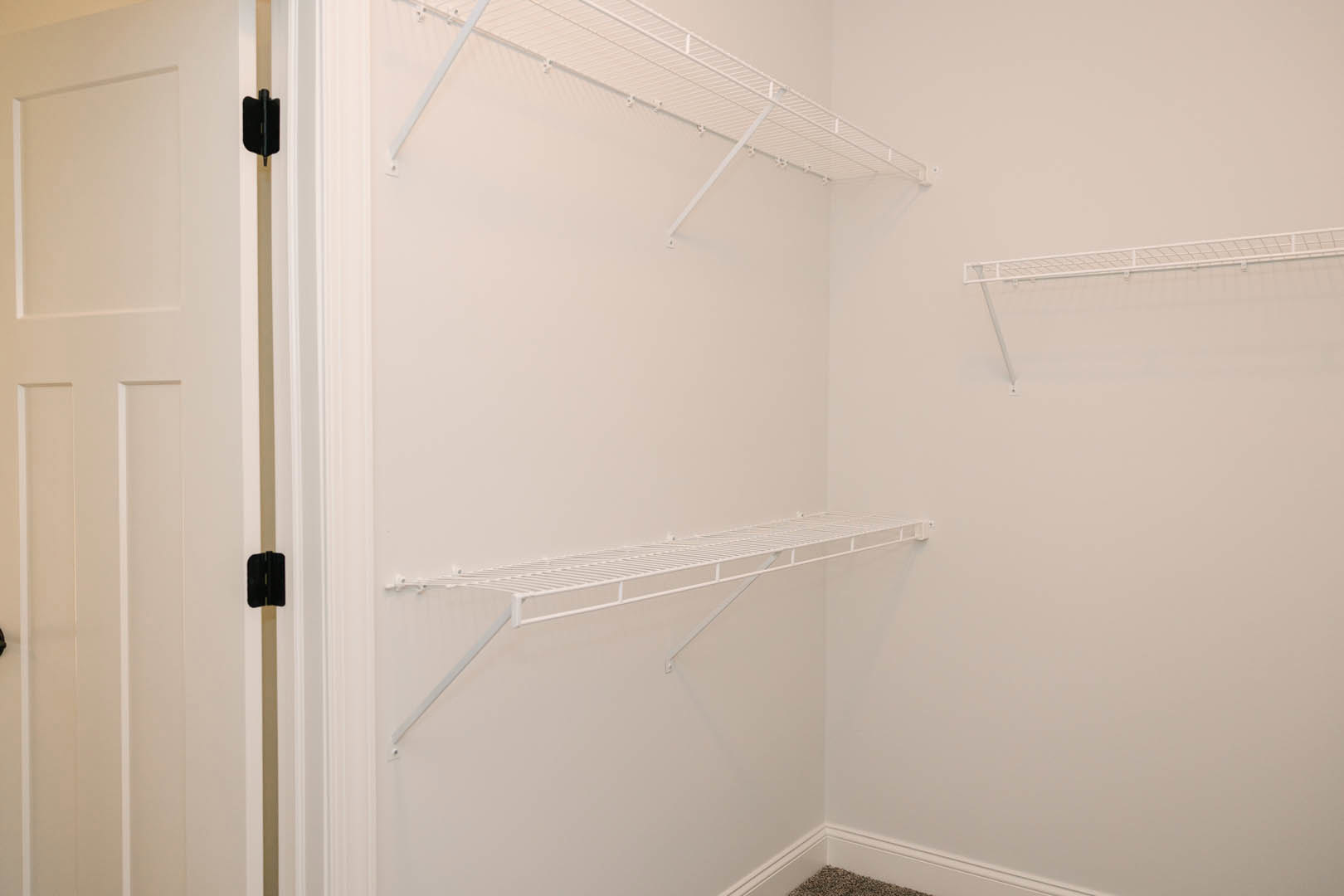 White built-in shelves with metal bars and hooks against a plaster wall, black rectangular objects with yellow and white accents, close-up of a white door with handle, indoor