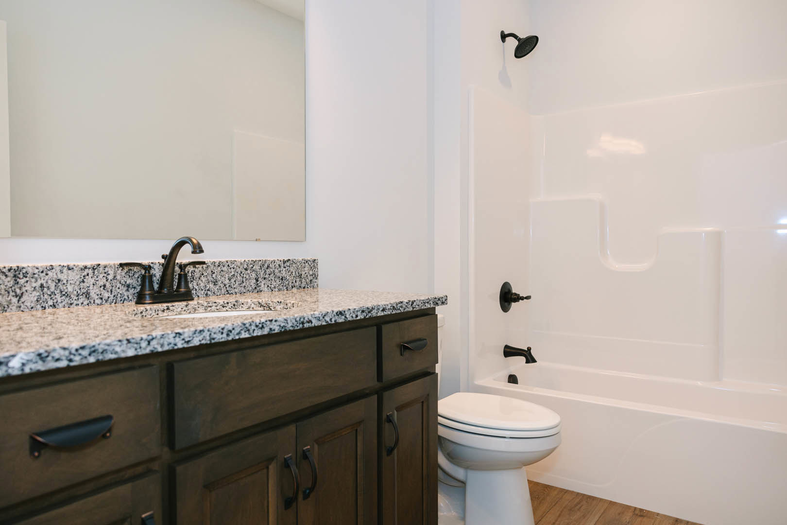 Modern bathroom featuring a marbled countertop with undermount sink, chrome faucet, black shower head against white tile wall, and closed toilet seat.