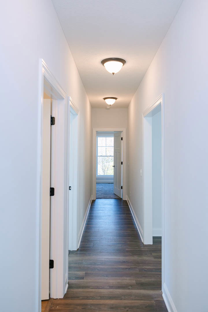 Hallway with white plaster walls, dark wood laminate flooring, white door with window, ceiling light fixture, and blue-framed window